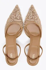 Zapato destalonado color beige con tacón fino y punta fina. Diseño de mesh con bordados florales y detalle de pequeñas perlas.