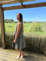 Vestido verde militar de lino, corte a la rodilla, sin mangas, con cuello mao y botones de nácar. Presenta varios cortes en su largo, aportando movimiento y un toque moderno a este diseño fresco y elegante.