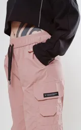 Pantalón cargo rosa con cintura elastizada y cordón ajustable. Botamangas ajustables con cordón elástico y tancas.