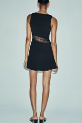 Vestido corto negro de cuello barco y sin mangas, con panel lateral de encaje floral transparente.