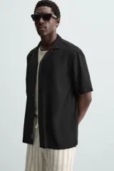 Camisa de calce relajado confeccionada en tejido fluido de mezcla de viscosa, color blanco. Presenta cuello bowling, manga corta, aberturas laterales en el bajo y cierre frontal con botones al tono.