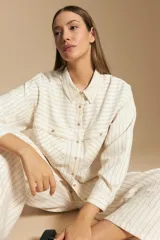 Camisa de manga larga color blanco hueso con finas rayas verticales en color oscuro. Presenta cuello camisero, botones frontales y dos bolsillos superpuestos en el pecho.