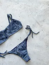 Conjunto de bikini con estampado a cuadros azul y blanco, compuesto por un corpiño bandeau con breteles regulables y una bombacha vedetina con tiras laterales para atar.