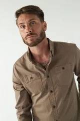 Camisa de hombre color marrón con efecto stone wash, fit regular, cuello americano, cierre con botones, dos bolsillos frontales con botón y mangas largas con puños abotonados.