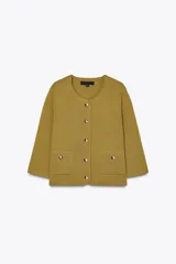 Chaqueta color mostaza de tejido de punto, con cuello redondo y manga tres cuartos. Tiene bolsillos delanteros de parche y cierre frontal con botones dorados.