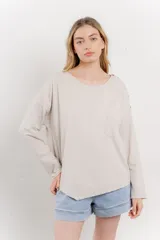 Remera color beige de corte holgado, con mangas largas, cuello redondo y bolsillo en el pecho. Presenta detalle de botones en el hombro.