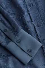 Camisa celeste con textura, cuello clásico, abotonada al frente, mangas largas con puños abotonados y bajo redondeado.