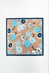 Pañuelo cuadrado de tela color tostado con estampado floral en tonos celeste, azul y blanco. Tiene un borde azul marino con una fina línea celeste.