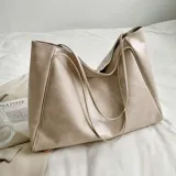 Bolso tipo tote bag color beige claro, de material sintético liso con caída suave. Posee dos asas delgadas para llevar al hombro.