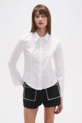 Camisa blanca de algodón, entallada, con cuello camisa y cierre frontal de botones. Presenta mangas largas con puños sencillos.