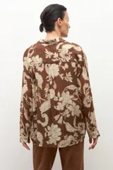 Camisa de manga larga con cuello y botones frontales, confeccionada en tela ligera con estampado floral en tonos marrón chocolate y beige claro.