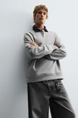 Sudadera gris de corte holgado, con cuello polo negro, cierre frontal de tres botones y mangas largas con puños acanalados.