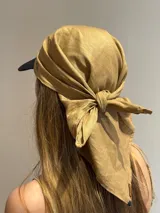 Pañuelo de cabeza de lino color mostaza, anudado en la parte trasera, usado sobre una gorra de visera negra.