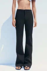 Pantalón negro de tiro alto con corte flare y cierre frontal con cremallera y gancho metálico.