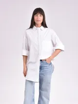 Camisa blanca de corte amplio, con cuello clásico, mangas 3/4 con puños arremangados y bolsillo de parche en el pecho.
