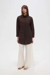 Camisa blanca de algodón con cuello clásico, corte holgado, cierre frontal con botones y mangas largas.