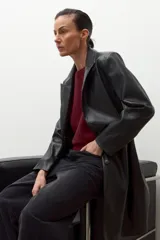 Blazer de mujer color negro, confeccionado en eco cuero, con solapas anchas, cierre frontal de un solo botón y pespuntes visibles.