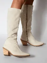 Bota alta color beige de cuero gamuzado, con punta fina y cierre lateral. Tiene un taco de madera con forma geométrica.