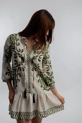 Vestido corto color crema con estampado de motivos geométricos en verde. Tiene cuello mao con lazo y borlas, mangas 3/4 y falda con volantes.
