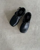 Zuecos negros de cuero con hebilla y tachas decorativas.