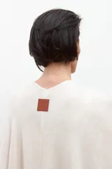 Capa tejida color crudo, de manga larga y corte amplio, con detalle de volados en los bordes.