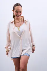 Camisa beige de corte amplio, con cuello clásico, cierre frontal con botones y mangas largas con puños abotonados.