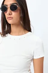 Remera blanca de punto acanalado con cuello redondo y mangas cortas. Presenta apliques de strass en el escote y las mangas.