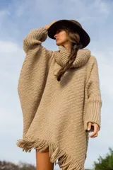 Poncho de tejido grueso color beige, con cuello alto y flecos en el ruedo.