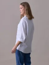 Camisa blanca de algodón con textura arrugada, cuello con solapa, abertura central con botones y bolsillo aplicado en el pecho. Mangas largas con largo regulable mediante presilla y botón.