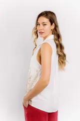Blusa blanca sin mangas con cuello camisero y bordado dorado con motivos vegetales en la parte inferior.