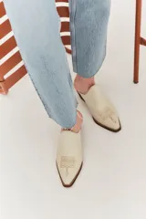 Mules de cuero color crema con punta fina y bordado estilo western en el empeine.