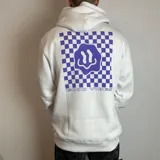 Canguro blanco con capucha y cordones ajustables. Estampado en la espalda con diseño de tablero de ajedrez en color violeta, un smiley face distorsionado y la frase "Good Vibes" en tipografía cursiva.