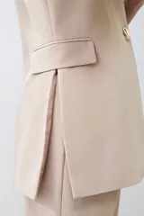 Chaleco largo color beige con solapas, sin mangas y con un botón metálico.