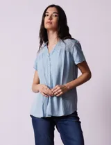 Camisa celeste de tencel con cuello con solapa, escote en V y abertura central con botones. Delantera con detalle en punto smock.