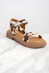 Sandalias con estampado animal print de vaca, con suela marrón y hebilla ajustable.