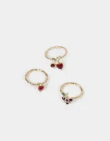 Set de tres anillos dorados con dijes de frutas con incrustaciones de strass: cerezas, frutilla y uvas.