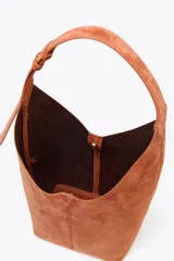Bolso tipo saca color marrón de piel, con asa al hombro y cierre imantado. Incluye cartera interior con cierre de cremallera metálica.