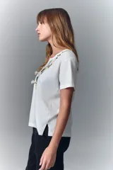 Remera negra de algodón con cuello redondo y mangas cortas. Presenta un estampado en el escote que simula un collar estilo boho con cuentas, borlas y dijes.