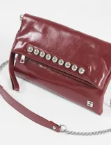 Sobre de mano color bordó, con textura símil cuero y tachas plateadas. Incluye correa de cuero y cadena metálica extraíble para usar como bandolera.