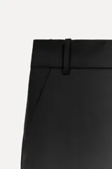 Pantalón negro de tiro alto con trabillas, confeccionado en mezcla de lana. Presenta bolsillos laterales, falsos bolsillos de doble vivo, cinturilla interior a contraste con pespuntes y raya planchada en el delantero. Cierre frontal con cremallera, botón interior y ganchos metálicos.