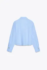 Camisa celeste de cuello redondo y manga larga, con lazo en el delantero y cierre frontal con botones.