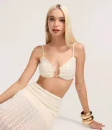 Blusa tipo crop top de color blanco hueso, con textura de tejido de punto y lentejuelas. Presenta escote corazón con un detalle metálico dorado en el centro que simula un cierre abierto. Tiene tirantes finos ajustables.