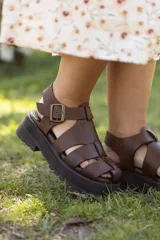 Sandalias de cuero marrón con diseño de tiras entrecruzadas y hebilla lateral. Plataforma track color negro.