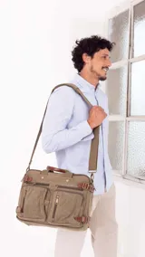 Mochila porta notebook de tela canvas color verde oliva con detalles en cuero marrón. Tiene correa de hombro ajustable y múltiples bolsillos con cierre.