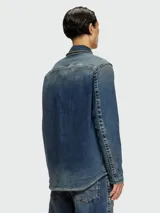 Campera de denim de lavado medio, con cuello camisero y cierre frontal. Presenta detalles de costuras marcadas y parches oscuros en los hombros.