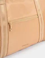 Bolso color beige de tela deportiva con manijas superiores y cierre superior. Tiene un bolsillo frontal con cierre y bolsillos laterales con cierre y tiradores de cordón y goma.