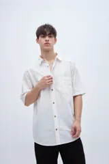 Camisa de manga corta en tela de algodón color blanco con rayas verticales en relieve y bolsillo en el pecho.