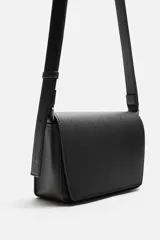 Bandolera negra con textura grabada, compartimento principal con cierre de solapa imantada, bolsillo interior con cierre y asa de hombro ajustable.