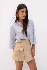 Minifalda beige de cuero con diseño cruzado, cinturón con hebilla metálica y bolsillo tipo cargo con solapa.