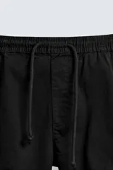 Pantalón cargo negro de corte slim fit, confeccionado en tejido de algodón con cintura elástica ajustable con cordón. Cuenta con bolsillos frontales, traseros y bolsillos tipo parche con solapa en los laterales.